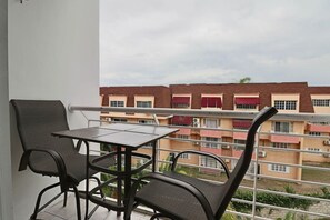 En balkon med et bord og stole, med udsigt over en boligbygning med flere vinduer og balkoner.