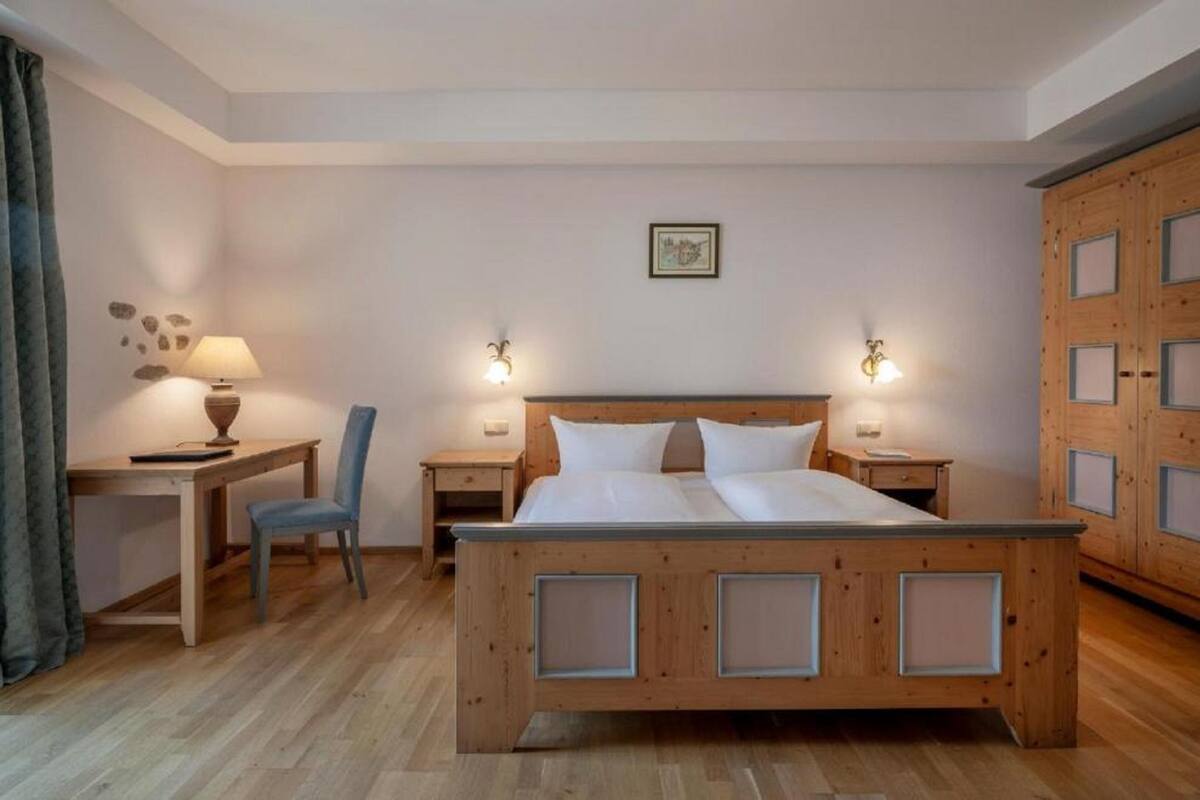 Un dormitorio con una cama de madera, dos mesitas de noche con lámparas, una silla, un escritorio y un armario.