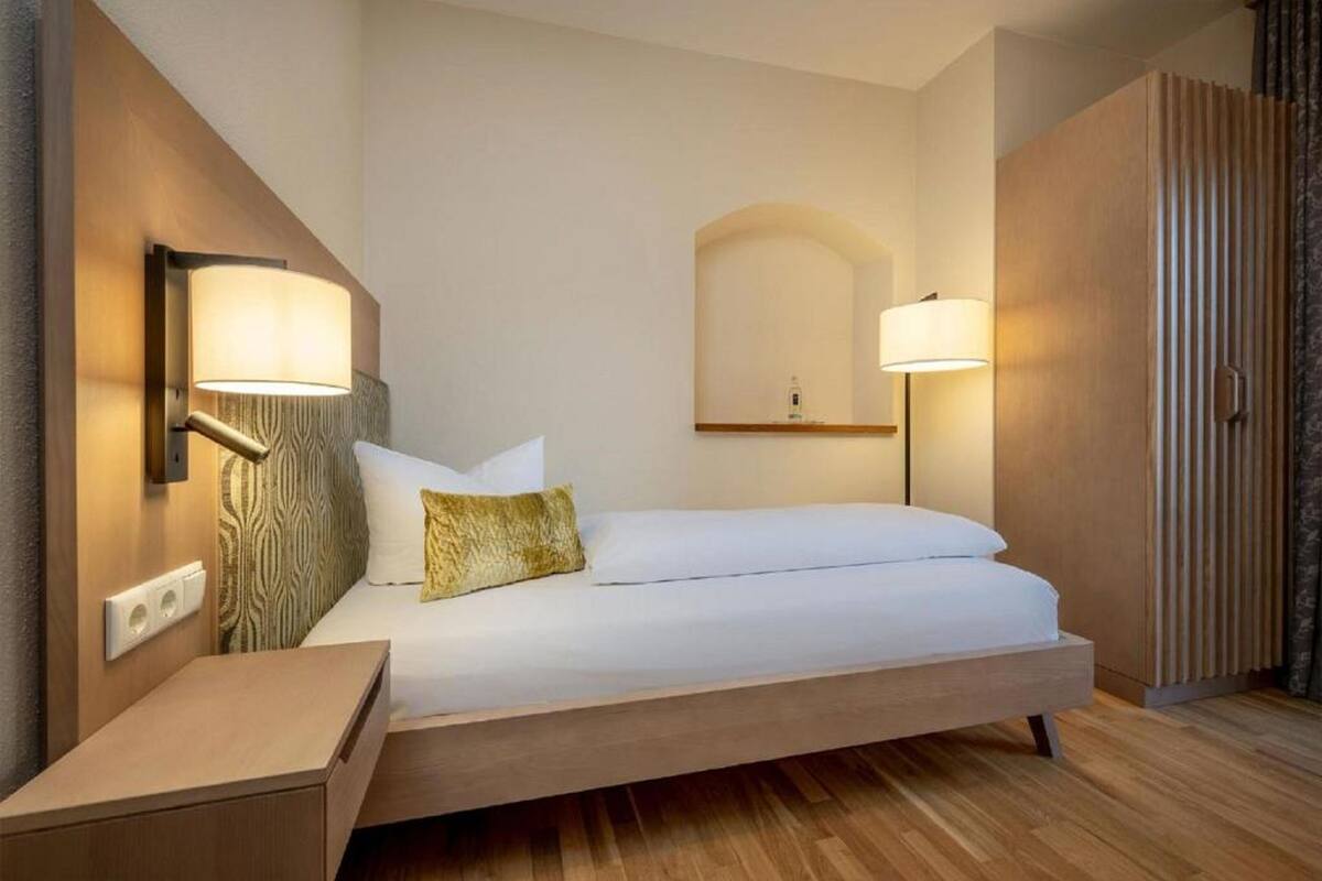 Una habitación de hotel moderna con una cama individual, lámparas de noche, una mesita de noche de madera y un armario empotrado.