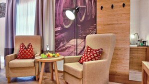 Une pièce comprenant deux fauteuils, une petite table ronde avec des fruits, un lampadaire et un mur en bois orné de motifs rappelant des tonneaux.