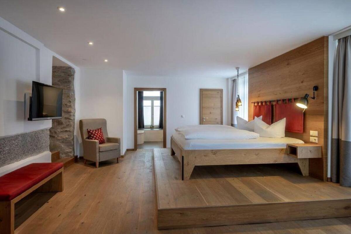 Un dormitorio con cama de madera, televisor montado en pared de piedra, una silla y un banco.