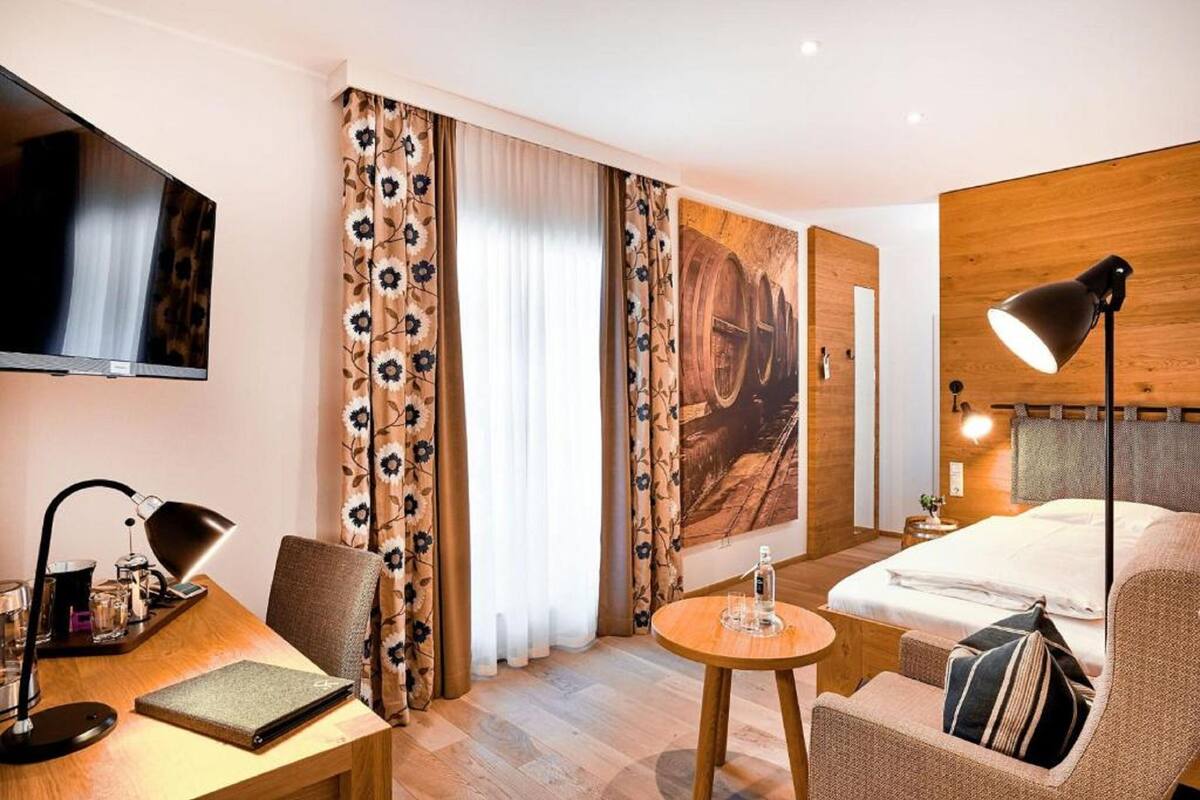 Habitación de hotel con cama, escritorio con lámpara, una silla, una mesa redonda y cortinas.