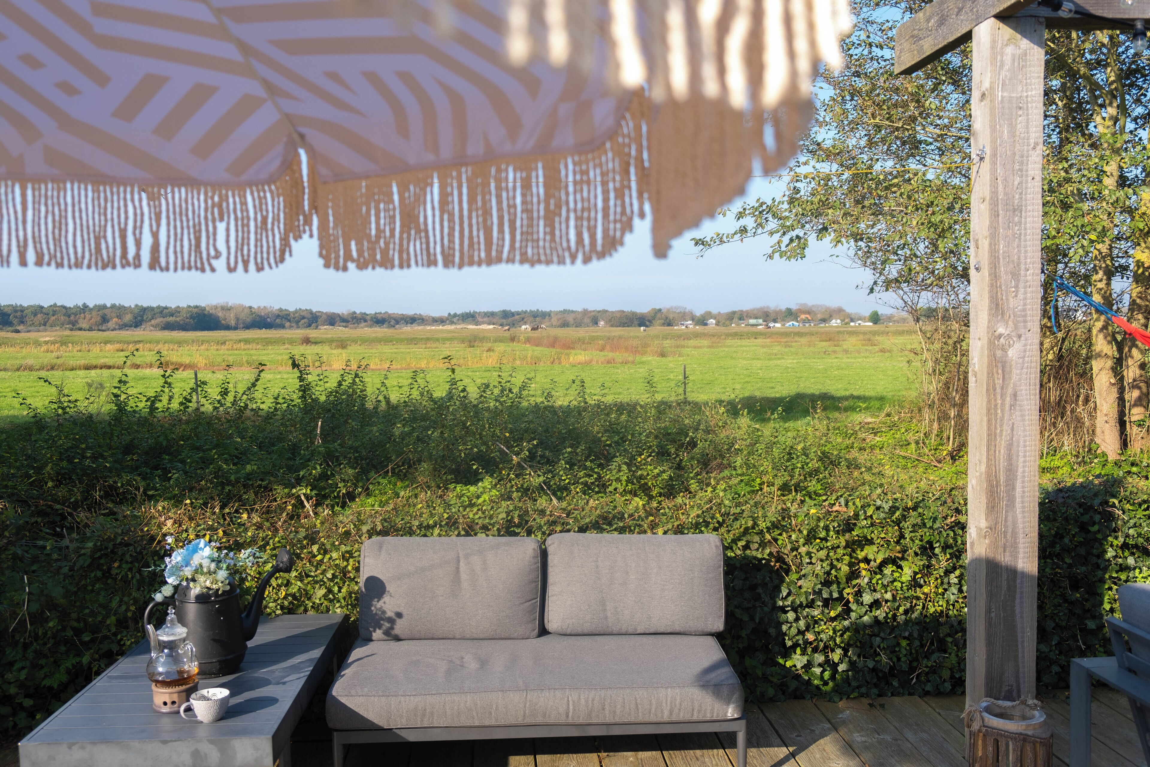 An outdoor seating area with a wooden table, a grey sofa, and a potted plant.
