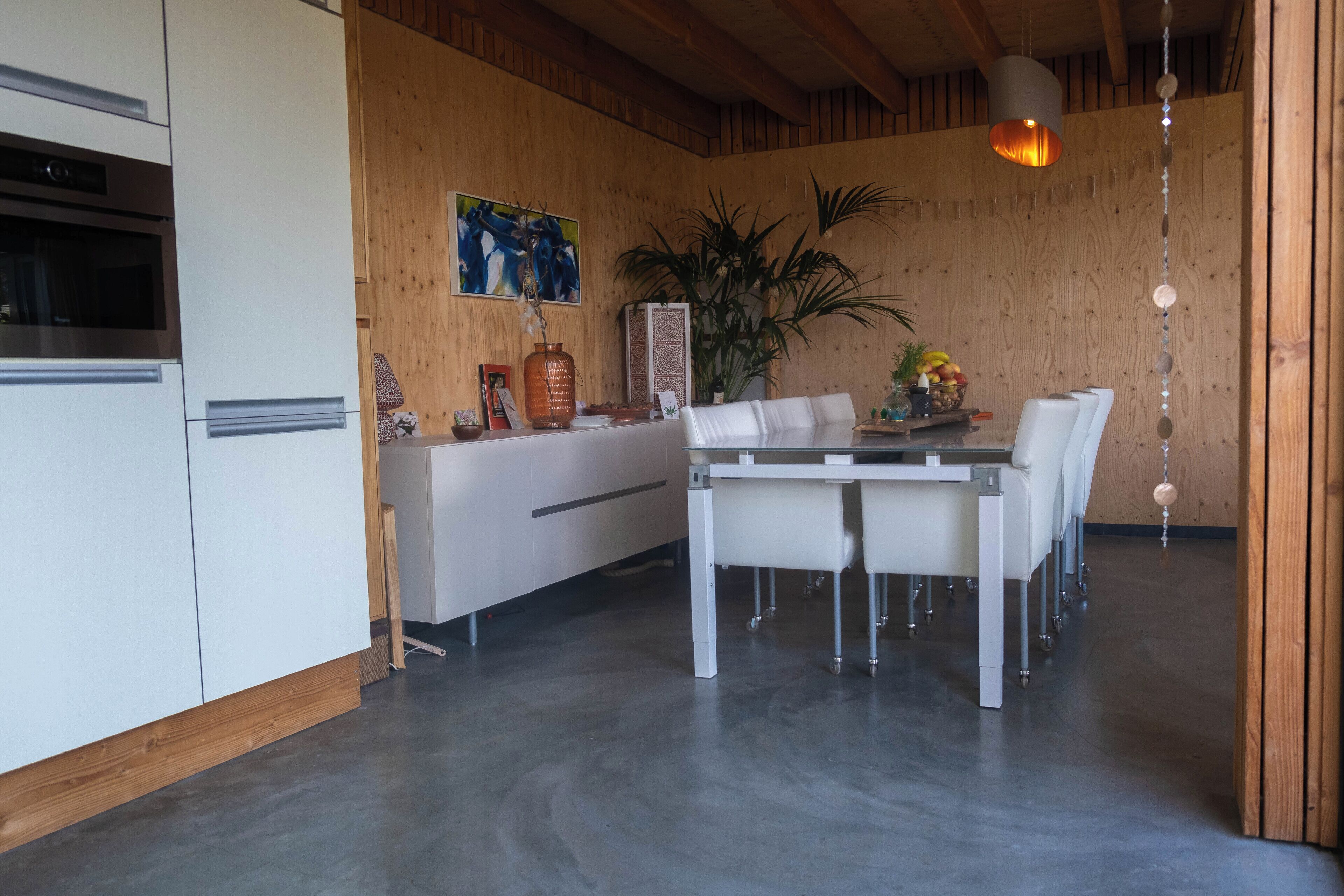 Une cuisine moderne avec des meubles blancs, un four encastré et un coin repas comprenant une table et des chaises blanches.