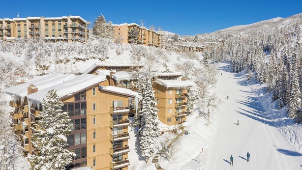 Ein verschneites Skigebiet mit mehrstöckigen Gebäuden, Skipisten und schneebedeckten Bäumen.