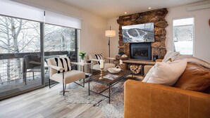 Ein modernes Wohnzimmer mit Kamin aus Naturstein, einem großen, an der Wand befestigten Fernseher und einer gemütlichen Sitzecke mit Ledersofa und Sesseln.