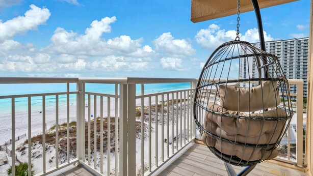 A balcony with a hanging chair overlooking a beach and a cityscape.