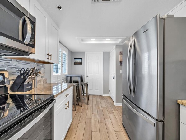 A modern kitchen with stainless steel appliances, a black countertop, and wooden flooring.