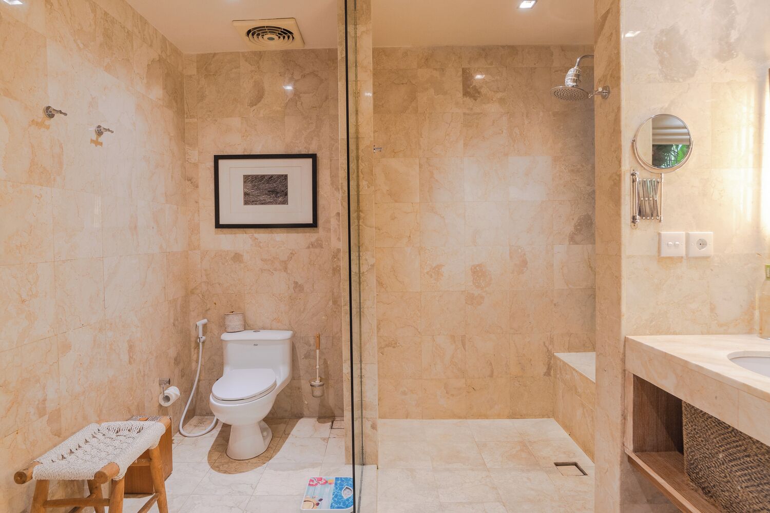 A bathroom with a glass shower enclosure, a toilet, a sink, and a framed picture on the wall.