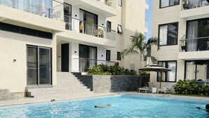 Un bâtiment moderne doté d’une piscine, d’un espace extérieur aménagé et d’un escalier menant à l’entrée.