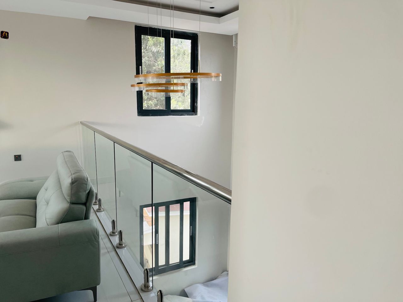 A modern living room with a glass railing, a sofa, and a hanging light fixture.