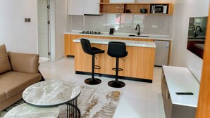 Une cuisine moderne dotée d’un îlot central, de deux tabourets de bar noirs, d’un plan de travail blanc et d’un micro-ondes encastré.