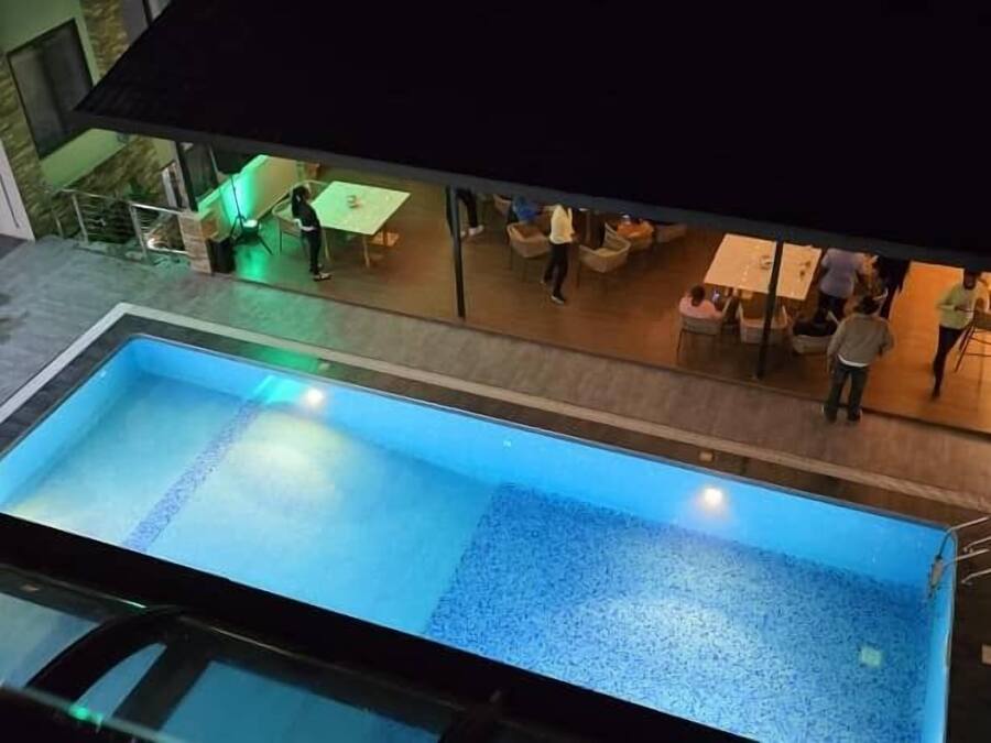 An indoor swimming pool with a tiled floor, surrounded by a lounge area with tables and chairs.