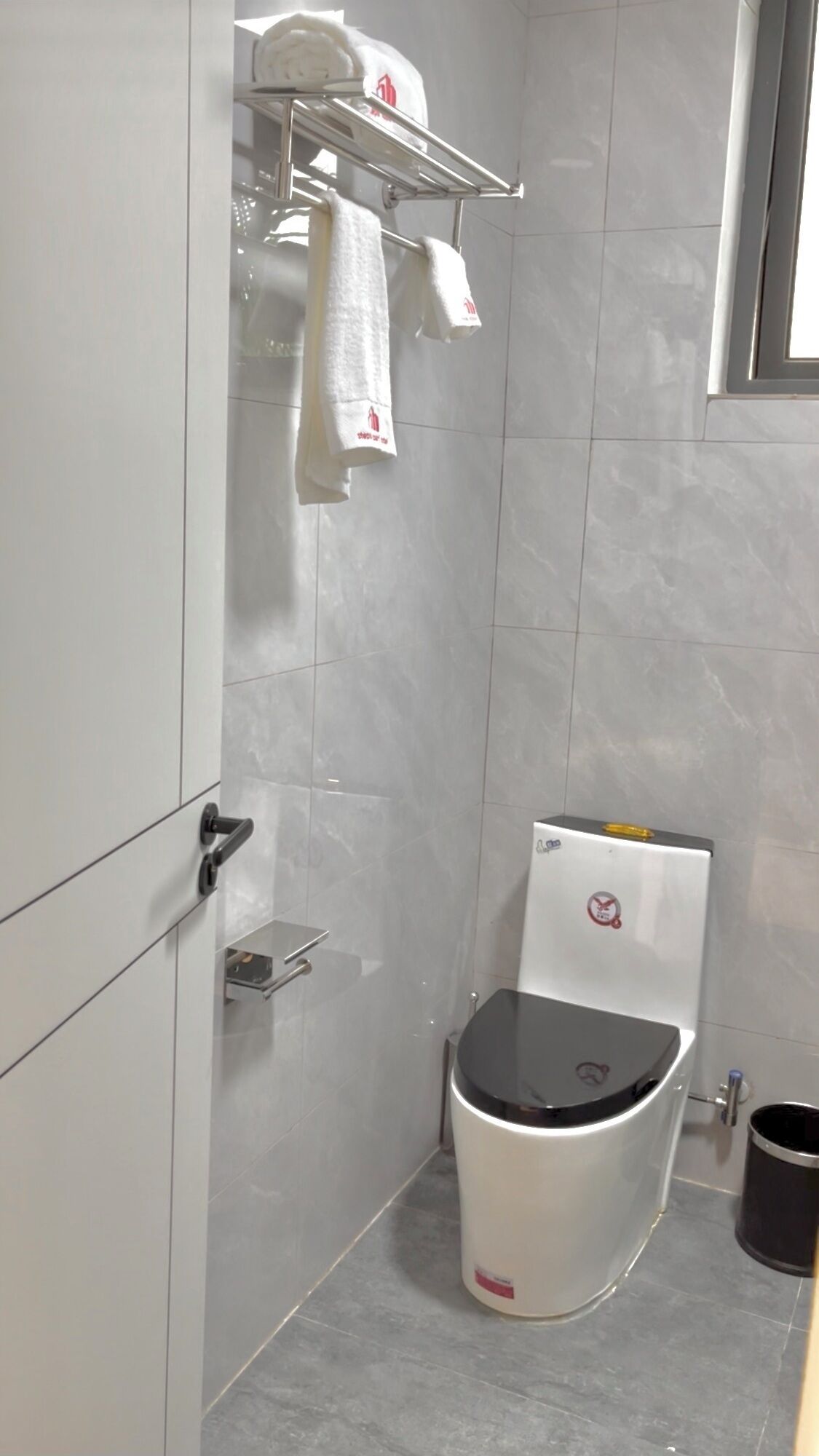 Un baño pequeño con inodoro, un perchero con toallas y un estante.