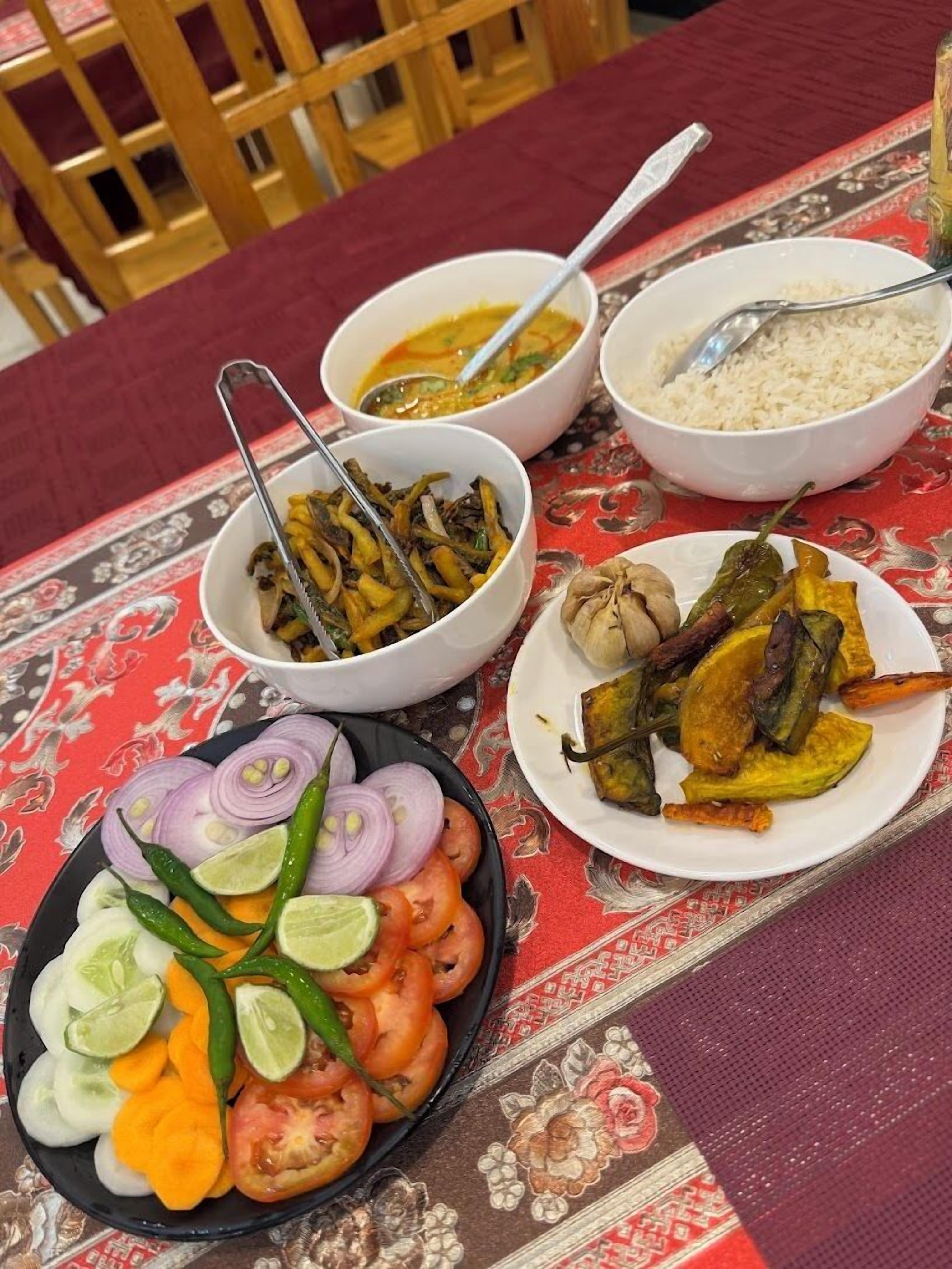Uma mesa com diversos pratos, incluindo arroz, vegetais e um prato com tomates e pepinos fatiados.