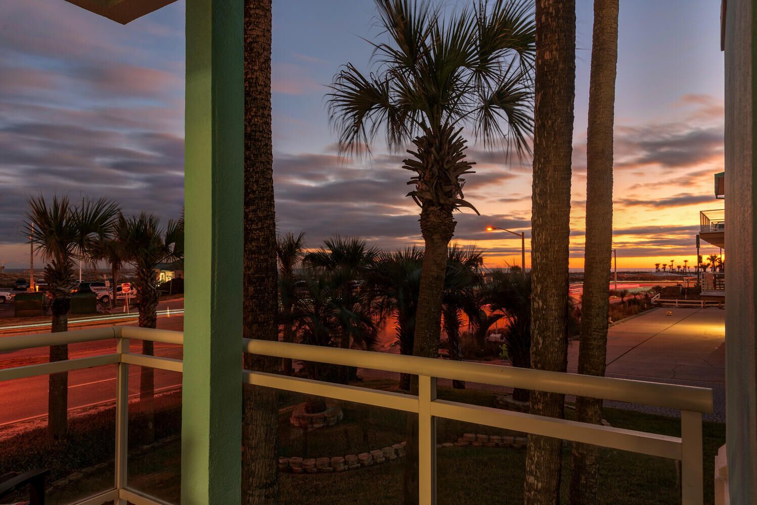 A balcony with a view of palm trees and a sunset.