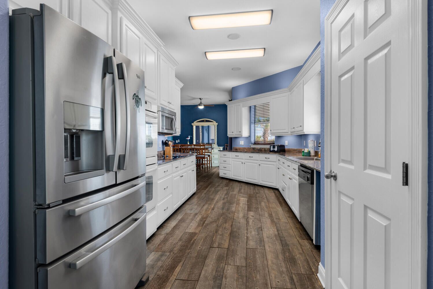 A modern kitchen with white cabinetry, stainless steel appliances, and a wooden floor.