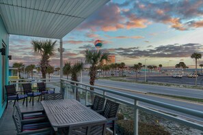 A balcony with outdoor seating, palm trees, and a view of a road and buildings in the distance.