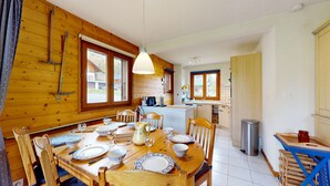 Een houten hut met een eettafel voor vier personen, een keuken met een spoelbak en fornuis, en grote ramen.