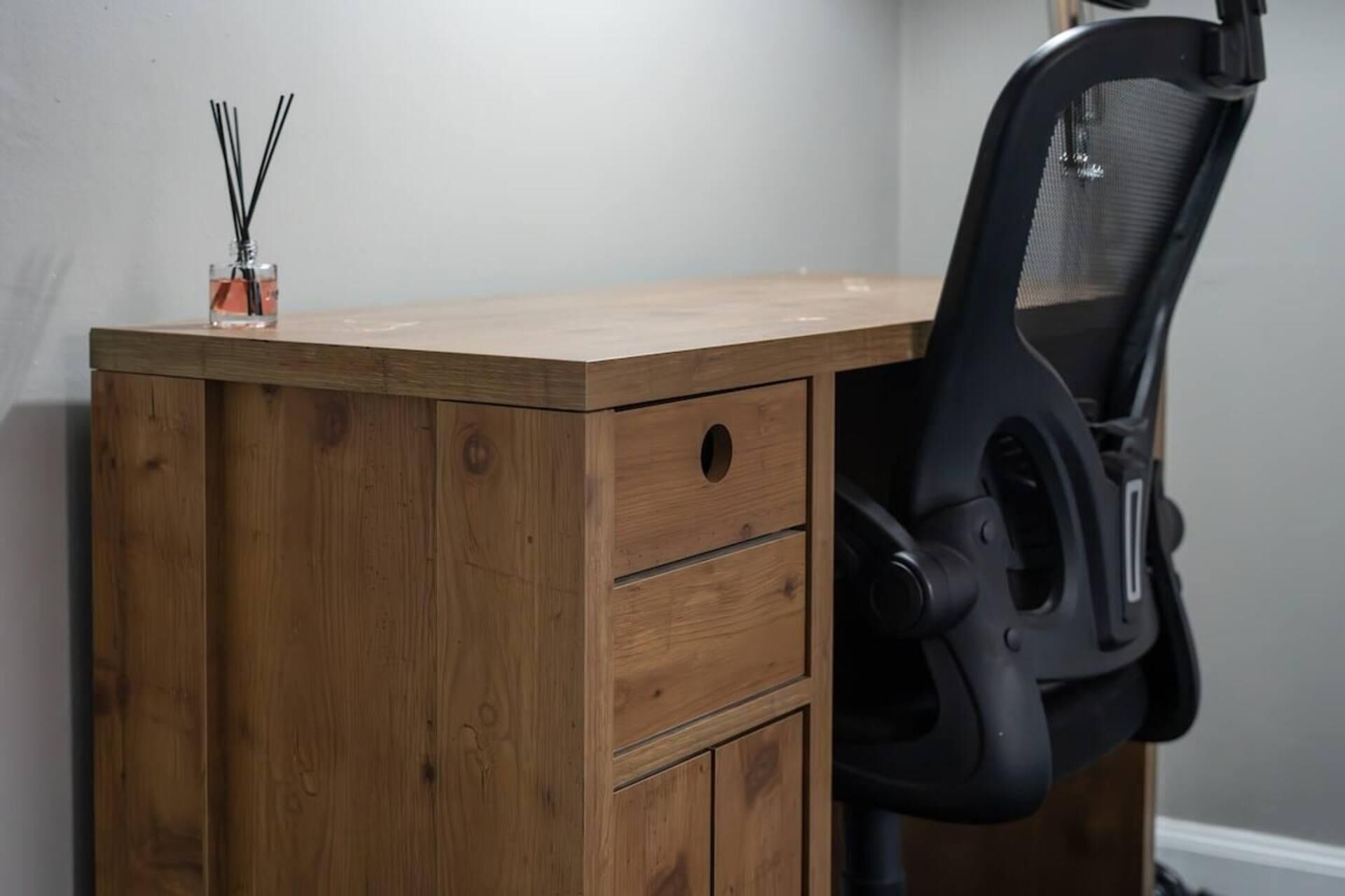 A wooden desk with a black office chair, a drawer, and a small container with reed diffusers.