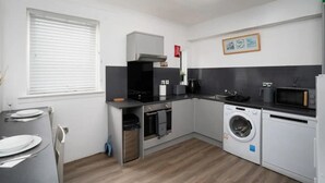 A compact kitchen with a microwave, washing machine, and a small dining area with a table set for two. - 2-bed Flat, Wishaw, Free Parking, Family-friendly (Wishaw)