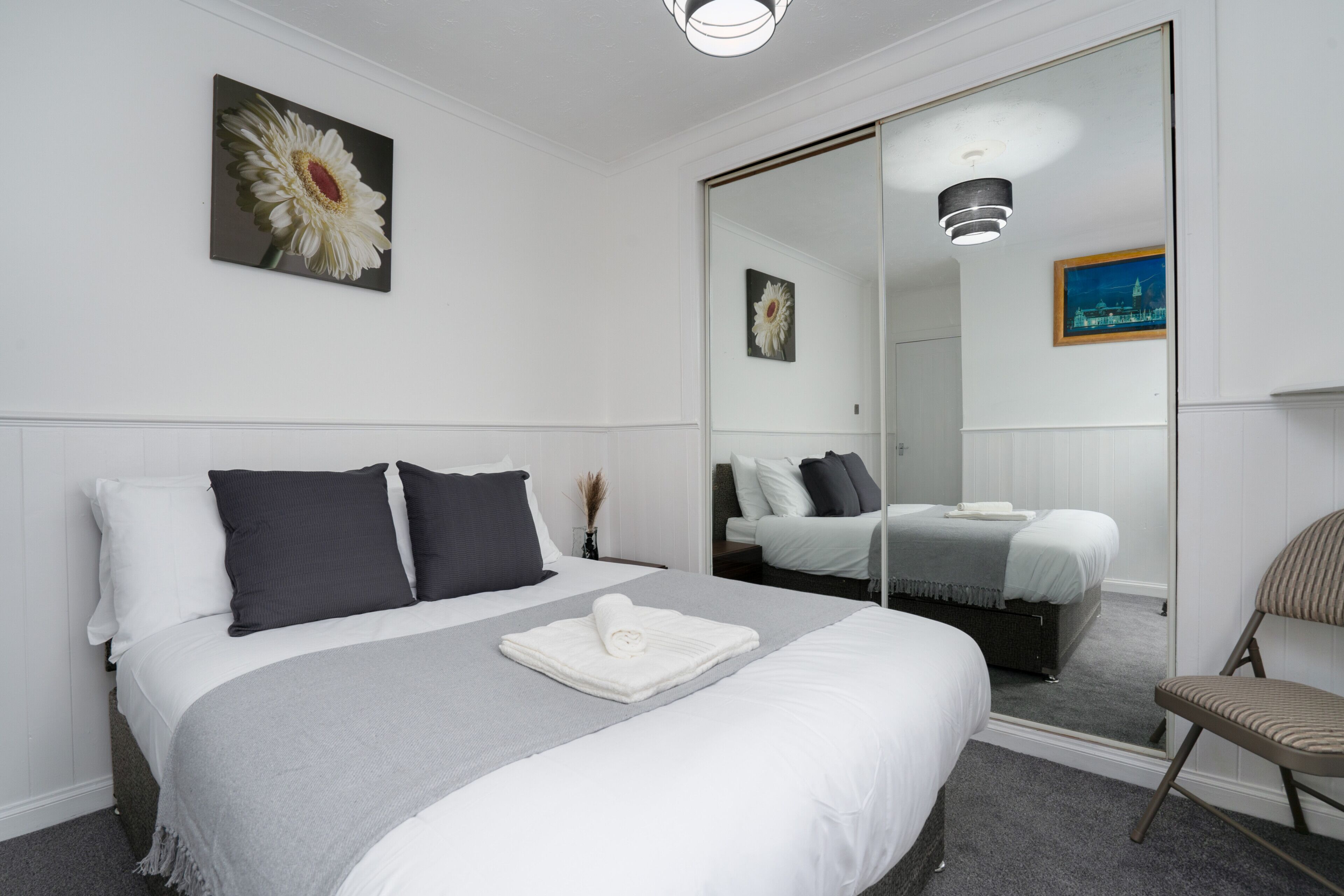 A neatly arranged hotel room with a large bed, a mirror, and a chair.