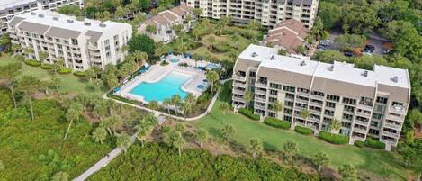 A high-rise hotel with multiple balconies, a central swimming pool, and lush greenery surrounding the property.