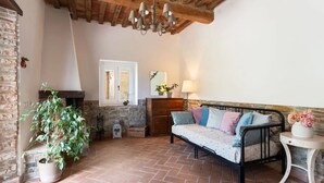 A cozy room with a stone fireplace, a bed with patterned bedding, a potted plant, and a wooden ceiling. - La Casa Del Tiglio (Borgo San Lorenzo)