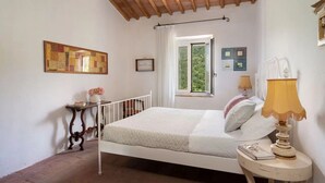 A bedroom with a bed, a bedside table with a lamp, a window with curtains, and a wall-mounted painting. - La Casa Del Tiglio (Borgo San Lorenzo)