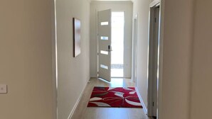 Ein Korridor mit Holzboden, einem rot-weißen Teppich und einer Tür zu einem hellen Raum.