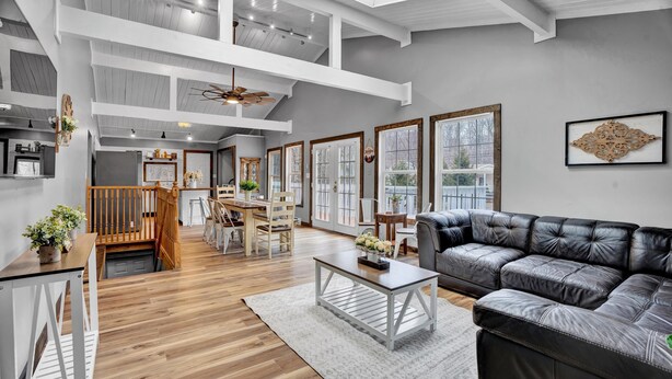 A spacious living area with a high ceiling, wooden floors, a black leather sofa, and a dining area with a wooden table and chairs. - Beautiful Poconos Getaway with Game room ,Hot Tub, and Fire pit (Tobyhanna)