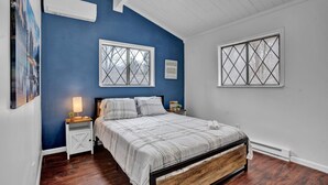 A bedroom with a bed, two nightstands, a wall-mounted air conditioner, and two windows with cross patterns. - Beautiful Poconos Getaway with Game room ,Hot Tub, and Fire pit (Tobyhanna)