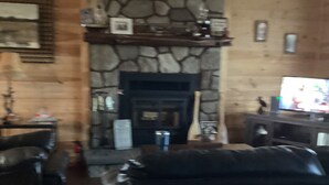 A living room with a stone fireplace, a ceiling fan, and a television.