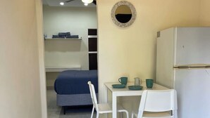 A compact kitchen with a white refrigerator, a small dining table with two chairs, and a mirror on the wall.