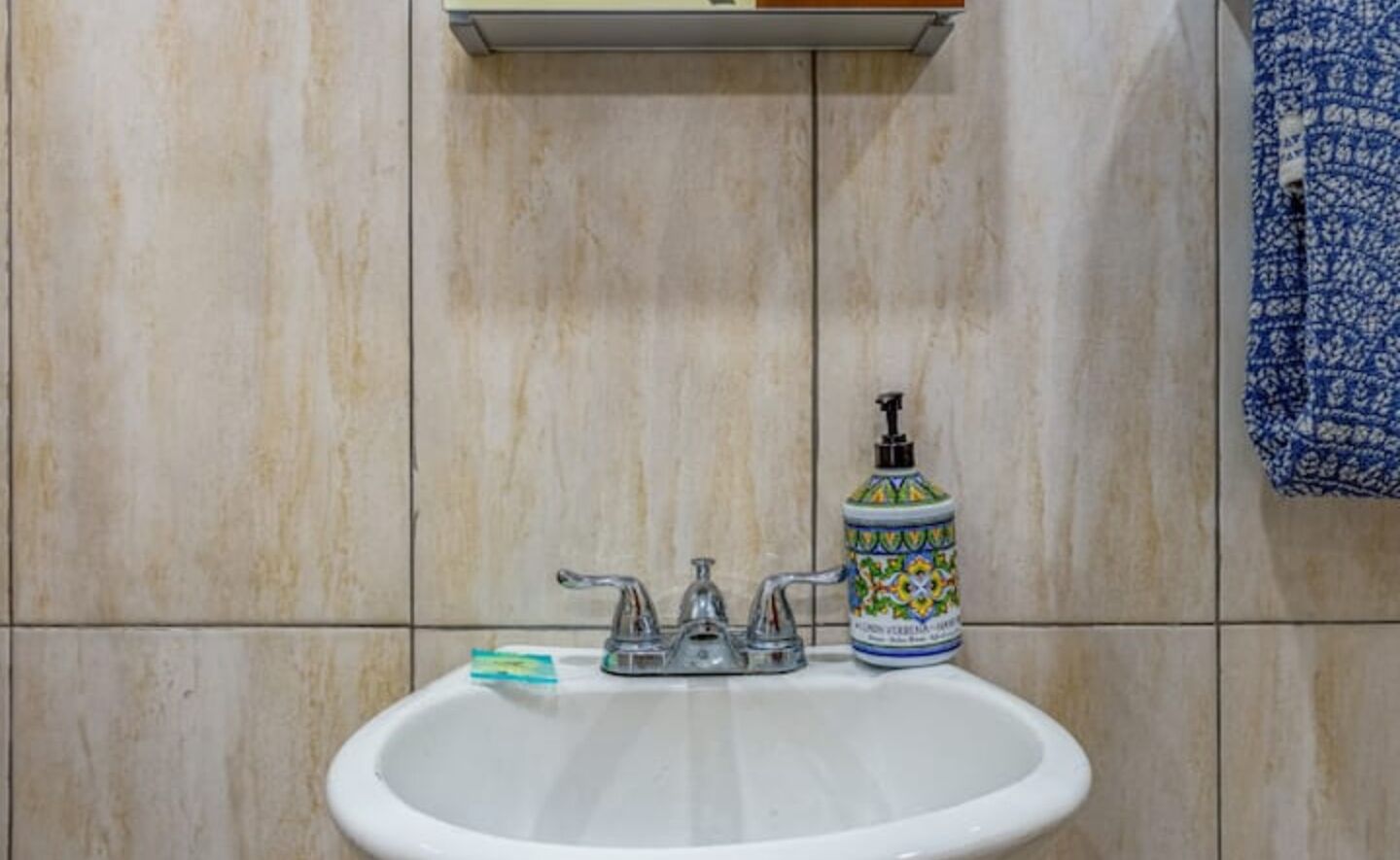 Ein Badezimmer mit einem weißen Waschbecken, zwei Wasserhähnen und einem Seifenspender auf der Ablagefläche.