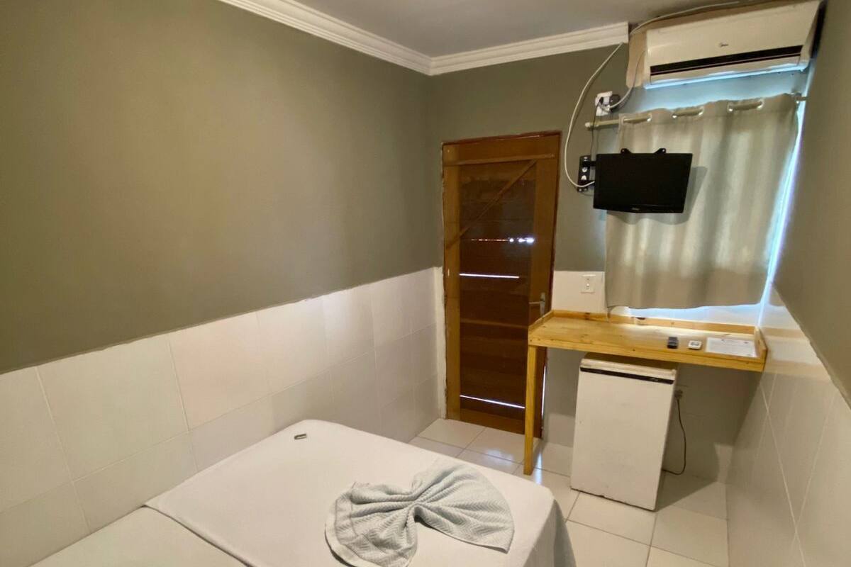 A small hotel room with a single bed, a desk with a TV, and an air conditioning unit.