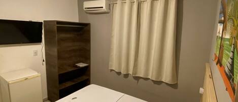 Una habitación de hotel con cama, un escritorio pequeño, un aire acondicionado y una cortina.