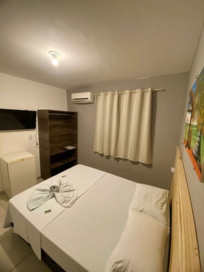 A hotel room with a bed, a small desk, an air conditioning unit, and a curtain. - Pousada Nascer do Sol  (João Pessoa)