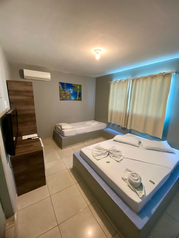 Une chambre d’hôtel avec un grand lit, un lit plus petit, un téléviseur à écran plat et un tableau au mur.