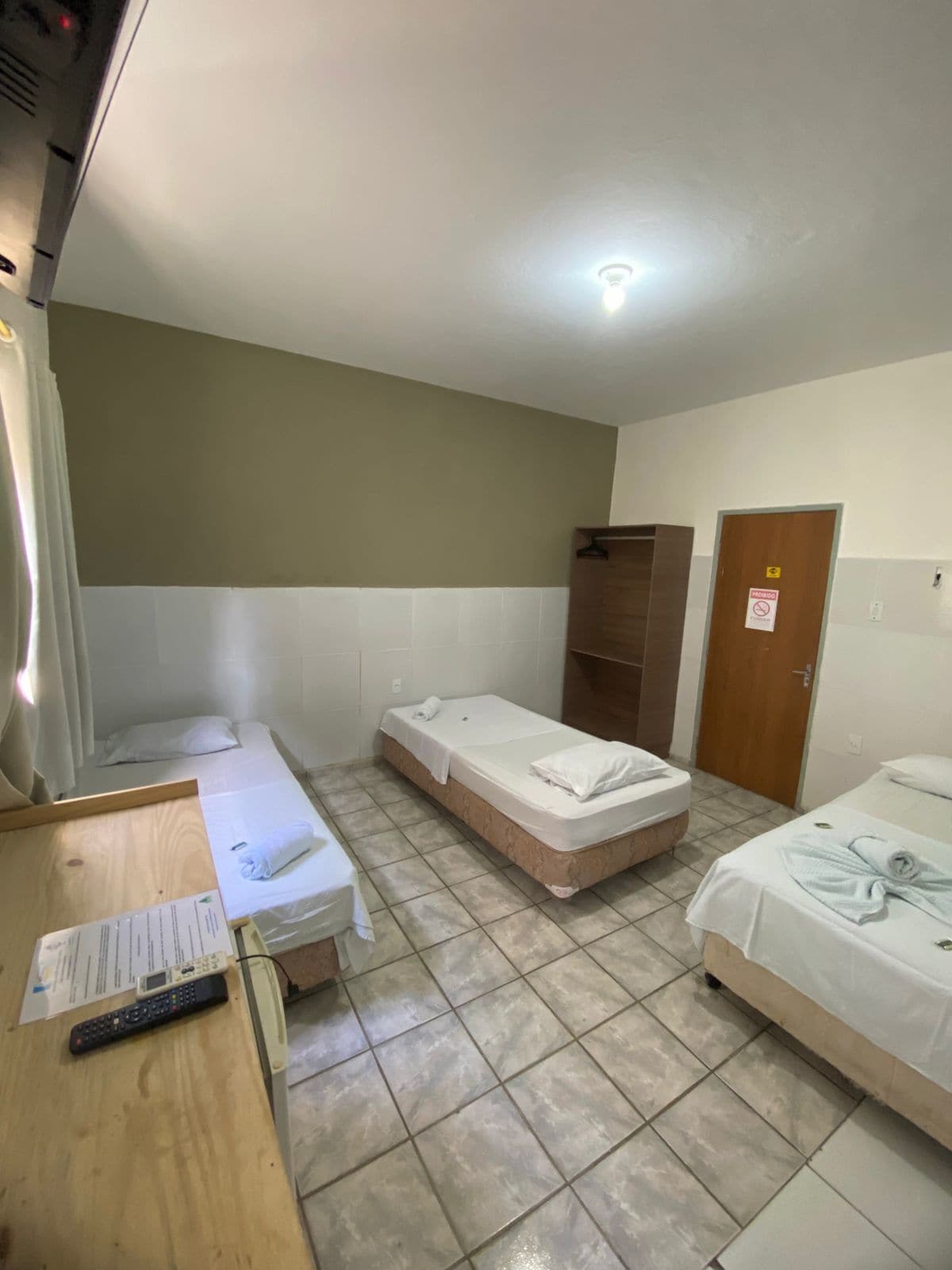 A hotel room with two single beds, a wooden desk with a telephone, and a door with a 'No Smoking' sign.