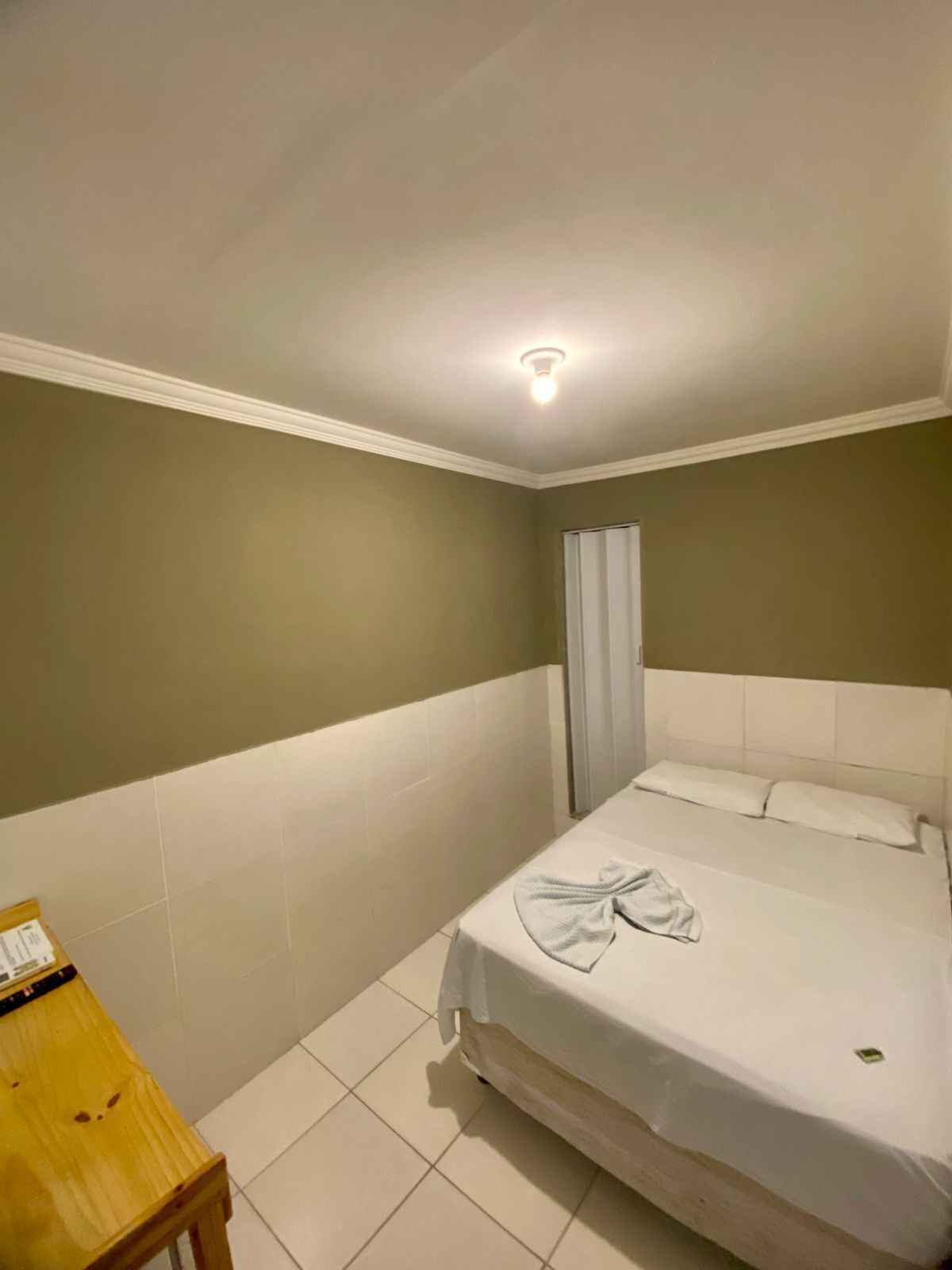Et lille, rent værelse med en enkelt seng, et trænatbord og en hvid loftslampe.