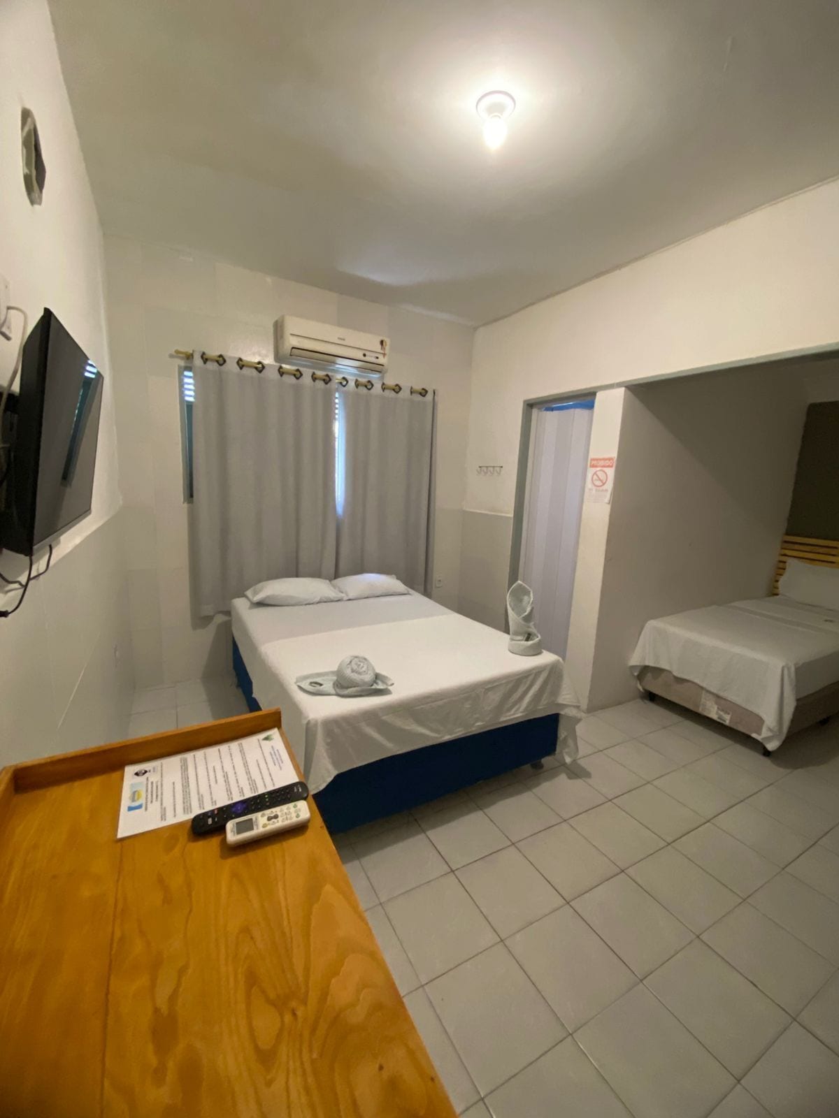 Una habitación de hotel con una cama, un escritorio con un control remoto y un televisor en la pared.