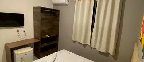 A bedroom with a bed, a TV, a small desk, and an air conditioner.