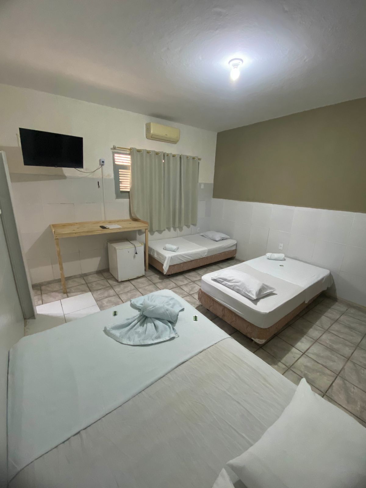 Una habitación pequeña y limpia con cama, escritorio, televisor y ventana con cortinas.