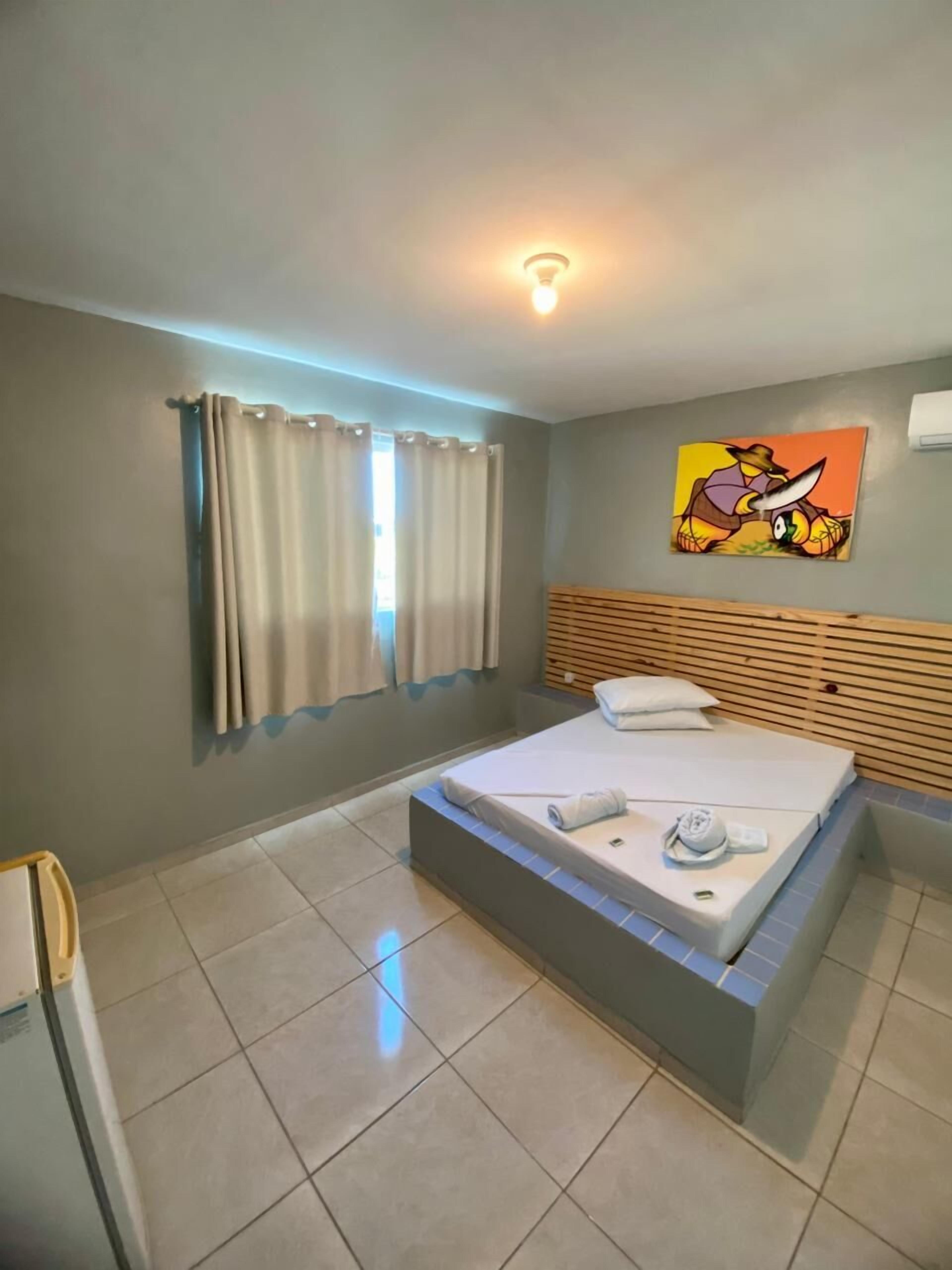 Quarto de hotel moderno com cama, cortinas, um quadro e uma luminária no teto.