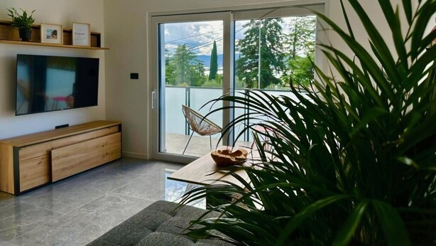 Una sala de estar moderna con televisor de pantalla plana, mueble de madera para entretenimiento y un amplio ventanal corredero que da a un balcón.