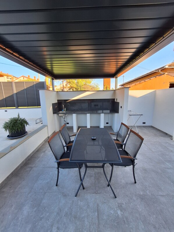 A covered patio with a grill, seating, and a potted plant. - Apartments E&T  (Ankaran)