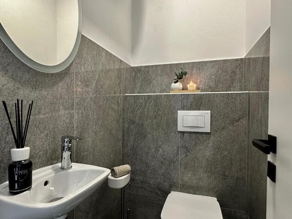 A modern bathroom with a white sink, a mirror, a towel, and a shower area.