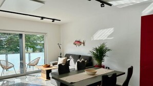 Una sala de estar moderna con un sofá, una mesa de comedor, sillas, una planta en maceta y un adorno de pez en la pared.