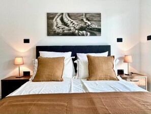 A neatly made bed with white and brown bedding, two bedside lamps, and a framed picture above the bed. - Apartments E&T  (Ankaran)